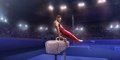 Male athlete doing a complicated exciting trick on a Pommel horse in a professional gym. Man...