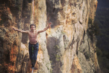 A man is walking along a stretched sling. Highline in the mountains. Man catches balance. Performance of a tightrope walker in nature. Highliner on the background of the mountains.