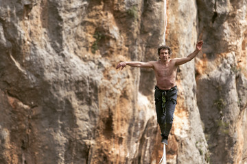 A man is walking along a stretched sling. Highline in the mountains. Man catches balance. Performance of a tightrope walker in nature. Highliner on the background of the mountains.