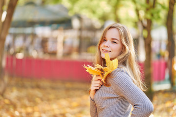 close-up portrait of a young woman with maple leaf in a park in golden autumn