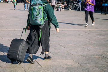 Unrecognizable young girl walking in the street with backpack and suitcase, travel and tourism concept