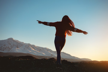 Slim girl with raised arms against sunset mountains