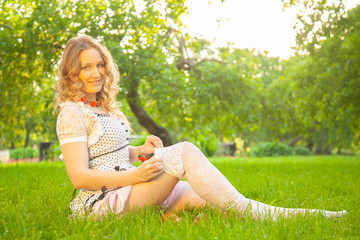 Naklejka na ściany i meble Young woman in white cute polka dot dress walking in an apple garden on a lovely sunny summer day