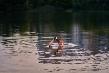 The girl in the shirt bathes in the river holds her hair
