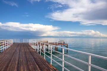 Obraz premium Pier on Issyk-Kul Lake on the background of a mountain range with snowy peaks and cloudy sky