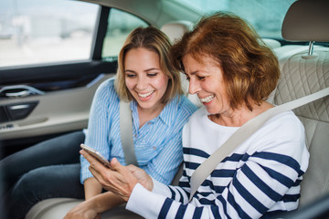 Cheerful adults sitting on back seats in car, using smartphone.