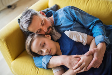 Mature father with small son lying on sofa indoors, sleeping and resting.