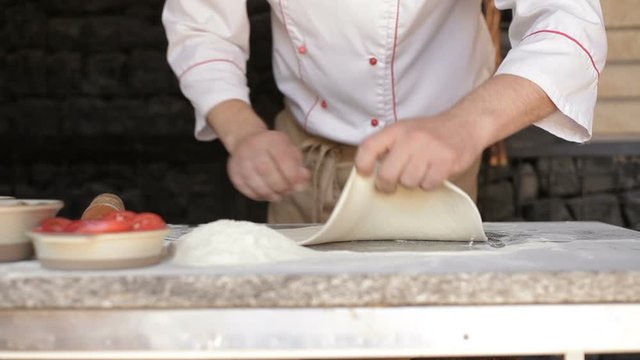 Chef in the restaurant rolls out the dough for traditional pizza