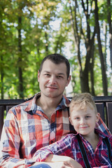 Handsome dad and son are sitting on a bench in the park.