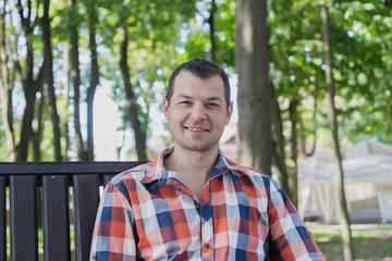 Young handsome man sits on a bench in a park.