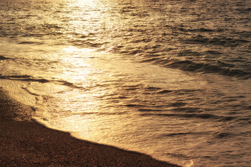 Sunset reflection on sea waves. Golden sunlight on waves of coastline. Sea beach at evening, summer vacation.