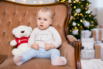 christmas concept - cute little baby girl sitting on vintage sofa near decorated christmas tree