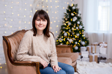 beautiful woman sitting on vintage sofa near decorated christmas tree