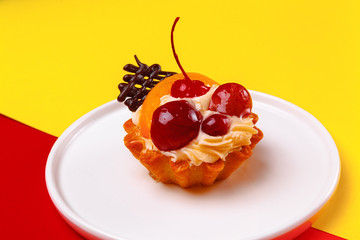 tasty cake, tartlet in a basket with whipped cream, berries and fruits, on a white plate. On a bright color background