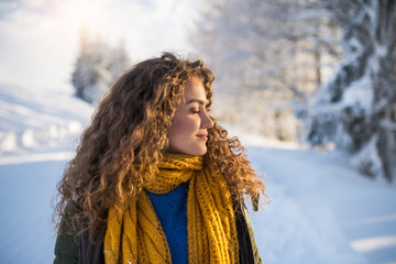 A front view portrait of young woman standing outdoors in snowy winter forest.