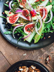 salad on a black matte plate: arugula, figs, avocado, red onions, cucumbers, walnuts, viburnum, thyme, spices