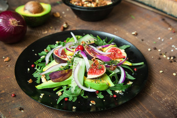 Fototapeta na wymiar salad on a black matte plate: arugula, figs, avocado, red onions, cucumbers, walnuts, viburnum, thyme, spices