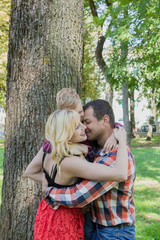Beautiful happy young family hugs by a tree in the park.