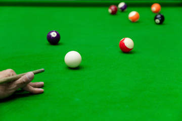 Man's hand and Cue arm playing snooker game or preparing aiming to shoot pool balls on a green billiard table.