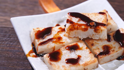 Pouring black soy sauce on ready-to-eat delicious turnip cake, Chinese traditional local dish radish cake in restaurant, close up, copy space.