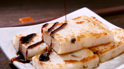 Pouring black soy sauce on ready-to-eat delicious turnip cake, Chinese traditional local dish radish cake in restaurant, close up, copy space.