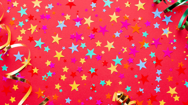 Festive red background with multicolor star confetti and streamers. Background for birthdays, christmas, anniversary
