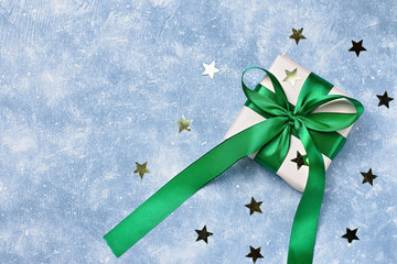 Green gift box with bow and golden confetti on blue background, copy space. Background for holiday