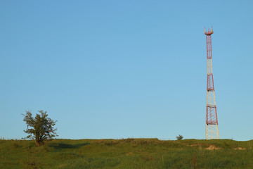 Fototapeta na wymiar Communications tower at the blue sky background and green meadow