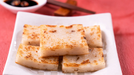 Chinese lunar new year food concept, Delicious turnip radish cake, local cuisine in restaurant with soy sauce on red background, close up, copy space