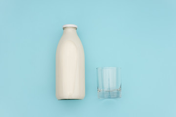 Milk in glass bottle and empty glass on blue background with copy space. Flat lay top view