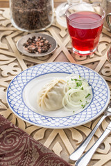 Dumpling with Onion and Butter on white plate and glass of red drink on oriental wooden table