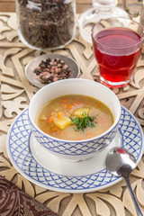 homemade vegetable soup with potatoes garnished with parsley and glass of red drink on oriental wooden table