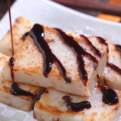Pouring black soy sauce on ready-to-eat delicious turnip cake, Chinese traditional local dish radish cake in restaurant, close up, copy space.