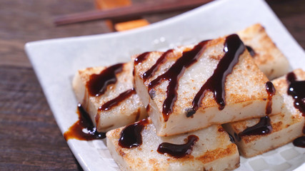 Pouring black soy sauce on ready-to-eat delicious turnip cake, Chinese traditional local dish radish cake in restaurant, close up, copy space.