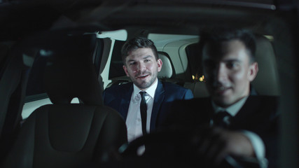 Two men drive in car and talk.