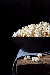 Popcorn in a black ceramic bowl on a wooden table against dark background