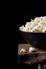 Popcorn in a black ceramic bowl on a wooden table against dark background