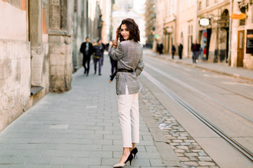 Attractive modern woman standing on the city street. Young beautiful girl in stylish elegant...