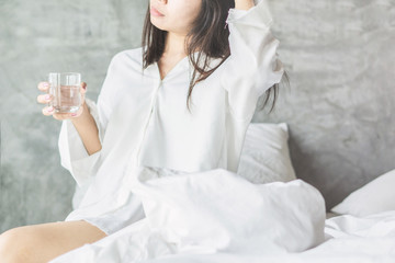 Asian woman drinking fresh water in bed after wake up in the morning 