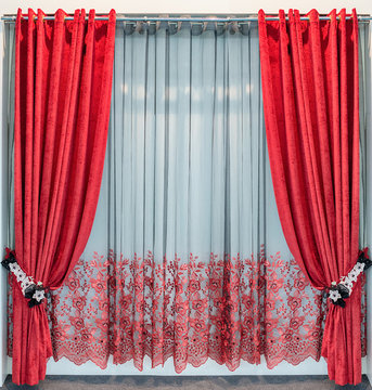Red velvet curtains with eyelets on a round metal cornice, tie-backs from lace flowers and the transparent tulle with embroidery