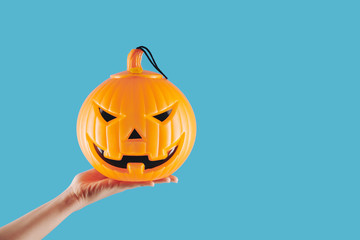 Hand of person holding plastic spooky jack-o-latern lamp for Halloween celebration, isolated on light blue