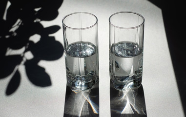Two glasses of water. Bright light and contrasting shadows.