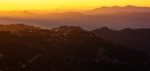 Fototapeta premium The setting sun lights up the hills above the city of Aizawl in yellow and orange hues.