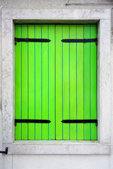 Green window shutters closed on a colorful wall in Burano near Venice, Italy