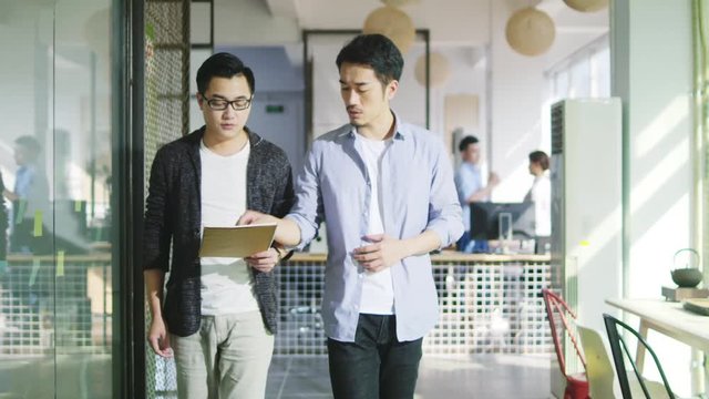 two young asian office worker discussing business while walking in company