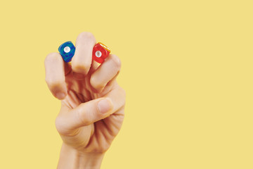 Fototapeta na wymiar Hand of person with red and blue dice between fingers on yellow background