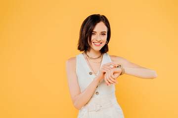 smiling elegant girl checking time on wristwatch isolated on yellow