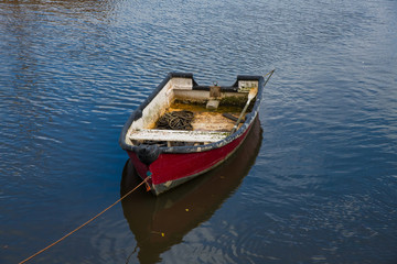 A worn red wooden rowing boat in a harbour