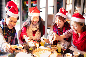 Happy friends having fun and celebrating christmas in hot pot restaurant