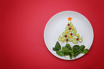 Creative edible vegan christmas tree, food art. Food for kids and festive table. Tree made from celery on a plate on red background.
